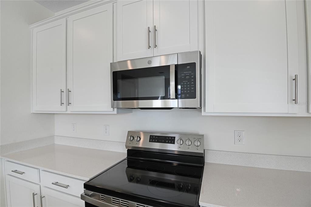 A kitchen features white cabinets, a stainless steel microwave, and a black electric range — 4056 BANNOCK AVENUE, TAVARES, FL