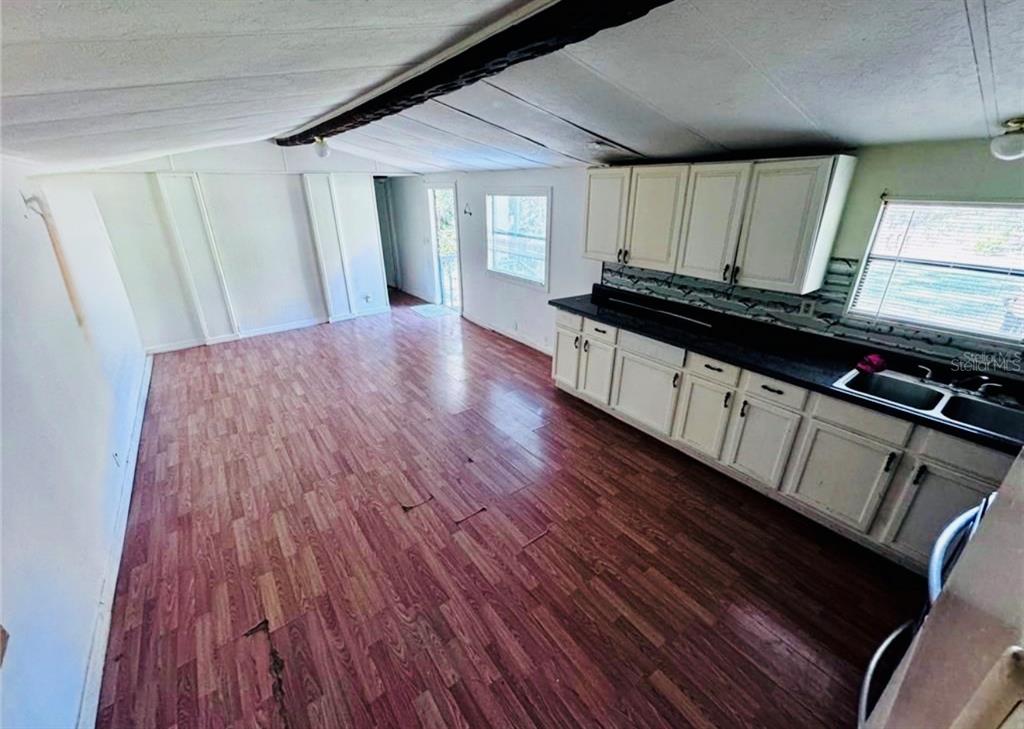 A kitchen with white cabinets and dark countertops opens into a living area with wood-look flooring — 13330 SW 9TH LANE, OCALA, FL