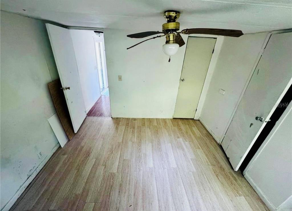 An empty room features light wood-look flooring, white walls, a ceiling fan, and multiple doors — 13330 SW 9TH LANE, OCALA, FL