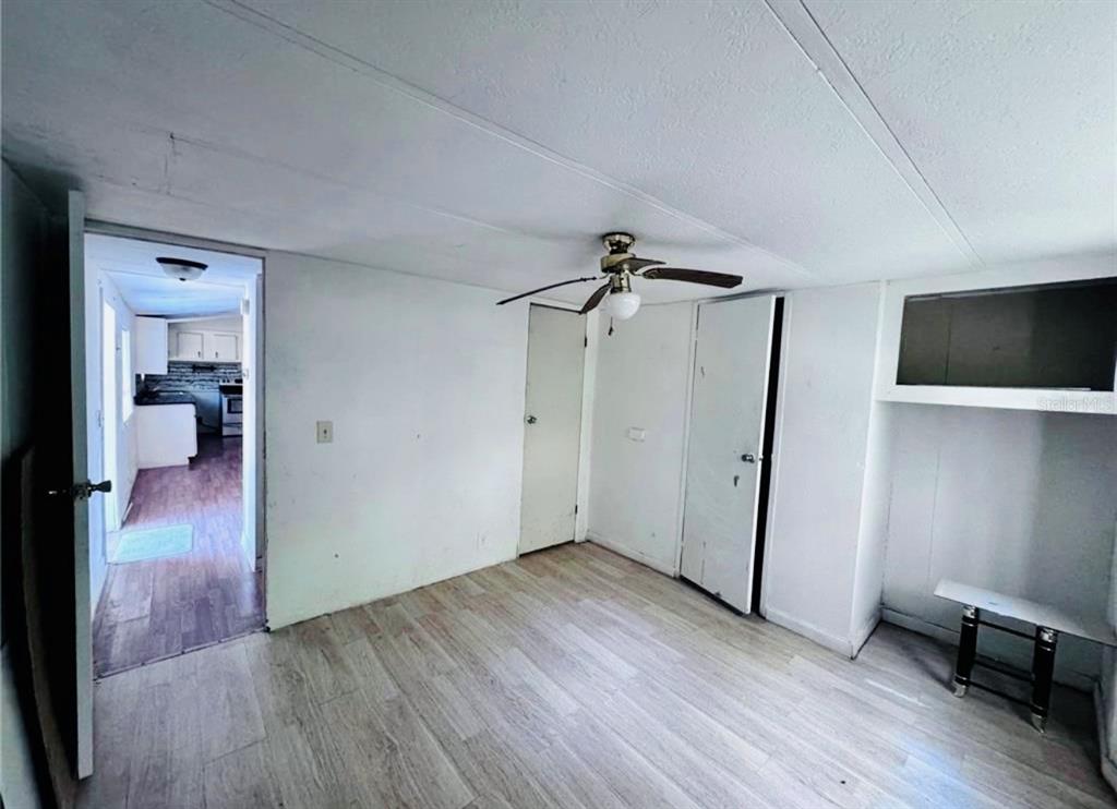 A room with light wood-look flooring, white walls, a ceiling fan, and two closed doors — 13330 SW 9TH LANE, OCALA, FL