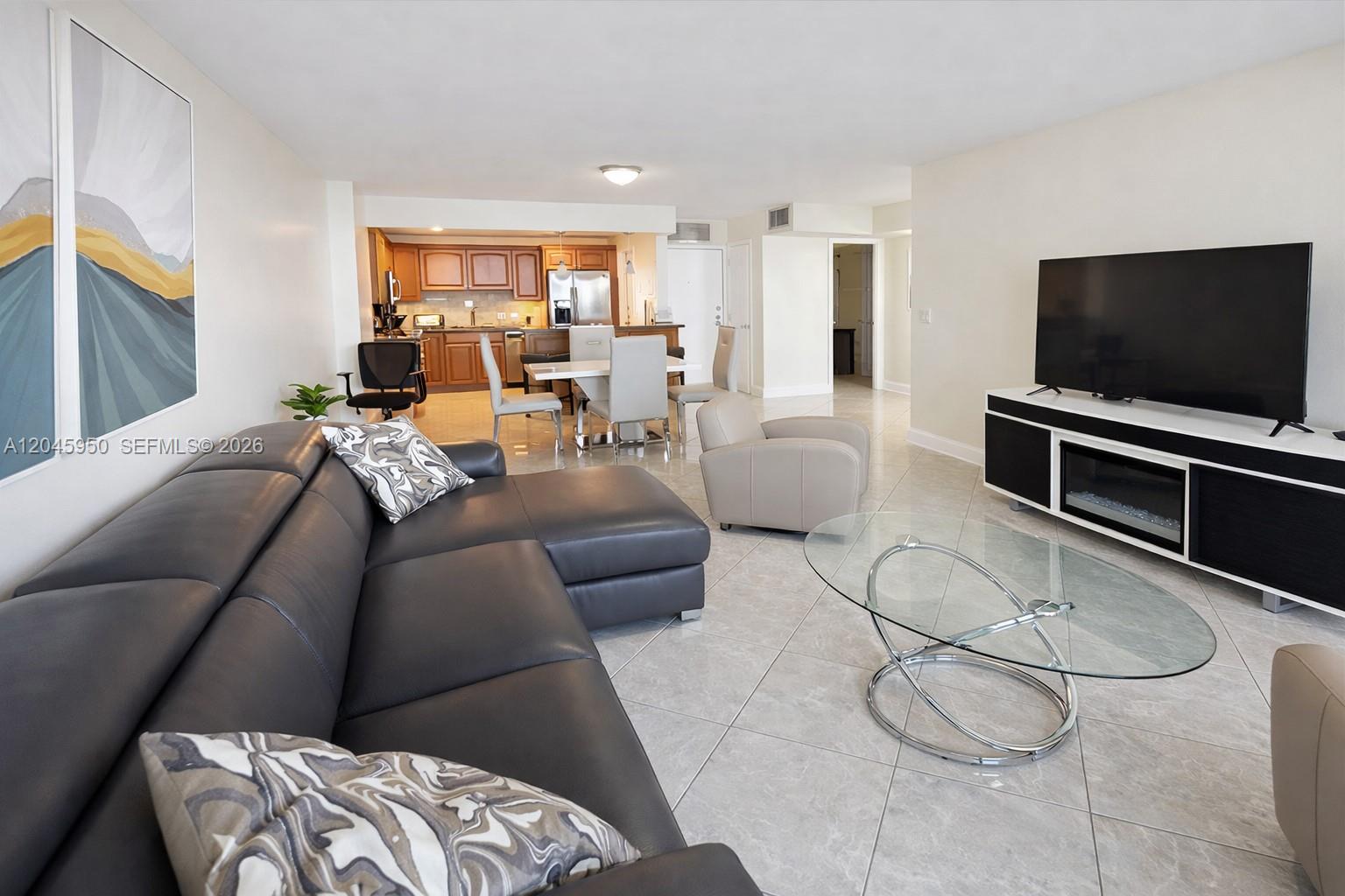 A living room with a dark sectional sofa, glass coffee table, and an open kitchen — 2101 S Ocean Dr # 606, Hollywood FL 33019, HOLLYWOOD, FL