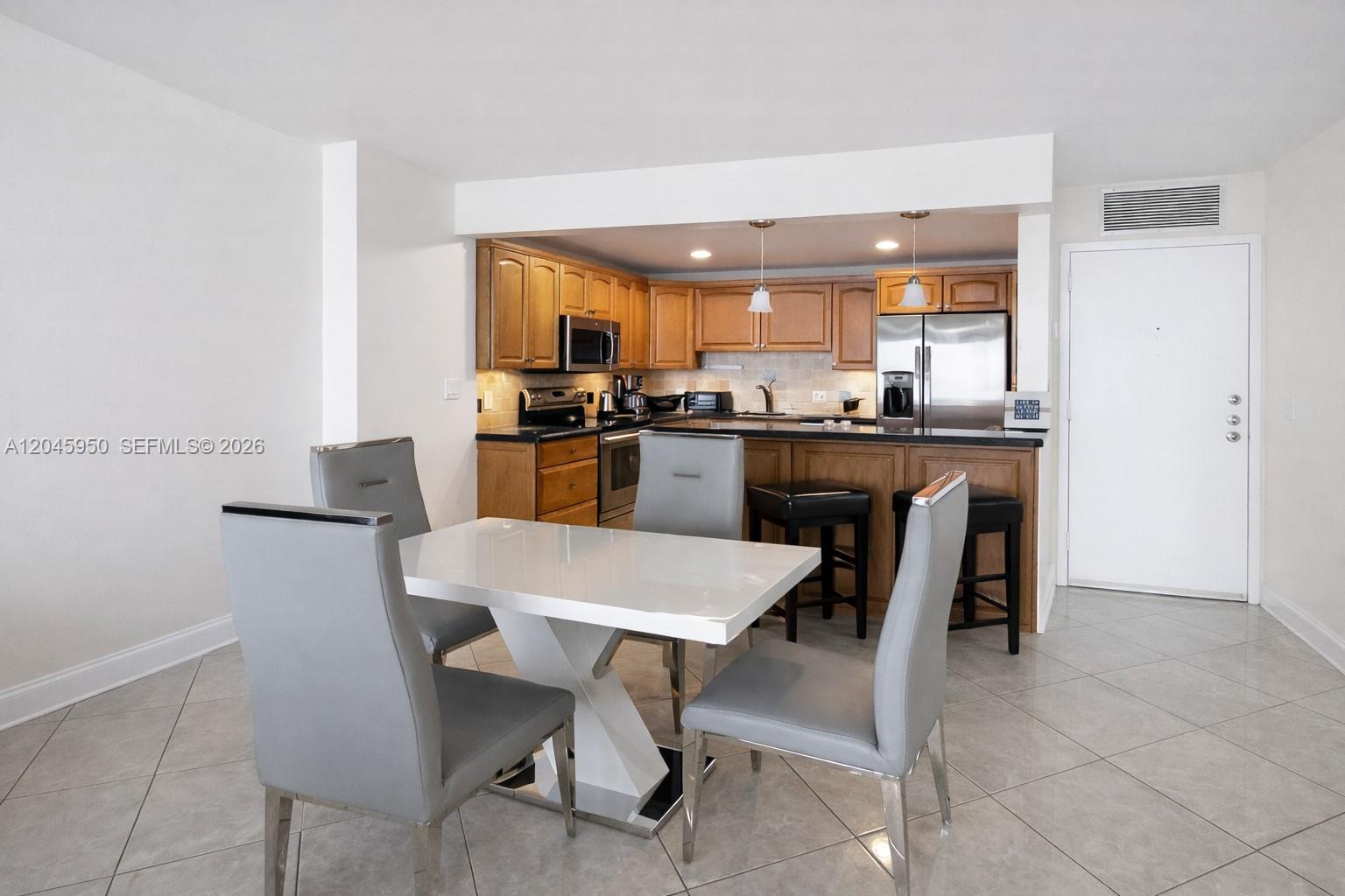 A dining area with a white table and grey chairs sits before a wood-cabinet kitchen — 2101 S Ocean Dr # 606, Hollywood FL 33019, HOLLYWOOD, FL