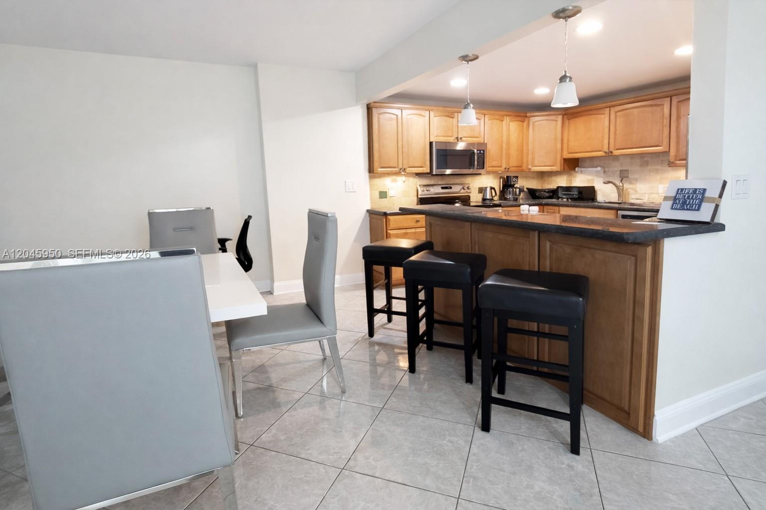 A kitchen with wood cabinets and a breakfast bar sits adjacent to a dining area — 2101 S Ocean Dr # 606, Hollywood FL 33019, HOLLYWOOD, FL