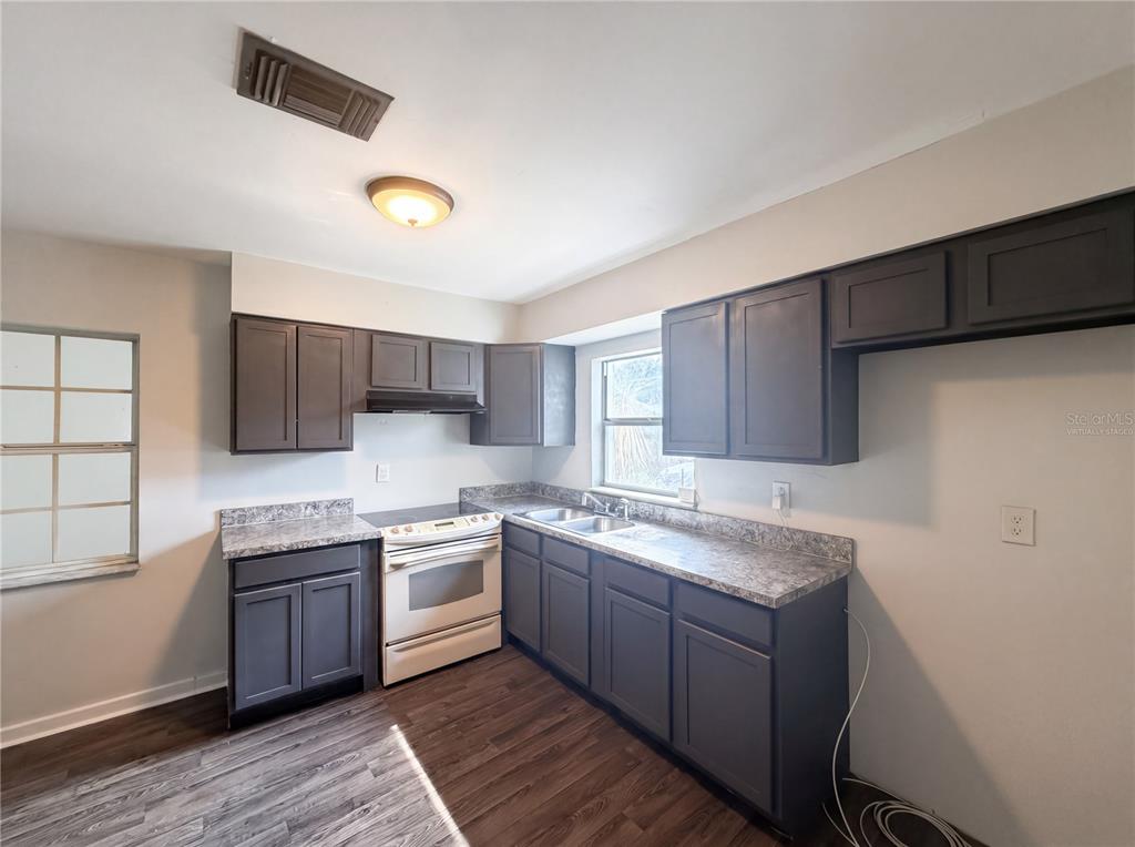 A kitchen features dark gray cabinets, laminate countertops, a white stove, and wood-look flooring — 1100 CAREFREE COVE DRIVE, WINTER HAVEN, FL