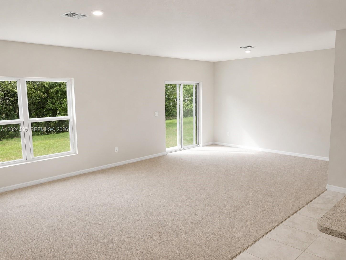 An empty living room features beige carpeting, neutral walls, a sliding glass door, and windows — 3327 Columbia Square Way, Fort Pierce FL 34982, FORT PIERCE, FL