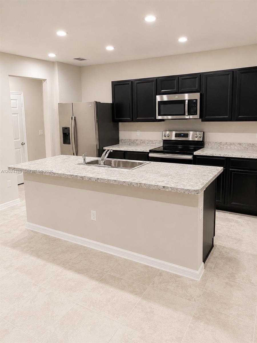 A kitchen features a central island, black cabinetry, stainless steel appliances, and light-colored countertops — 3327 Columbia Square Way, Fort Pierce FL 34982, FORT PIERCE, FL