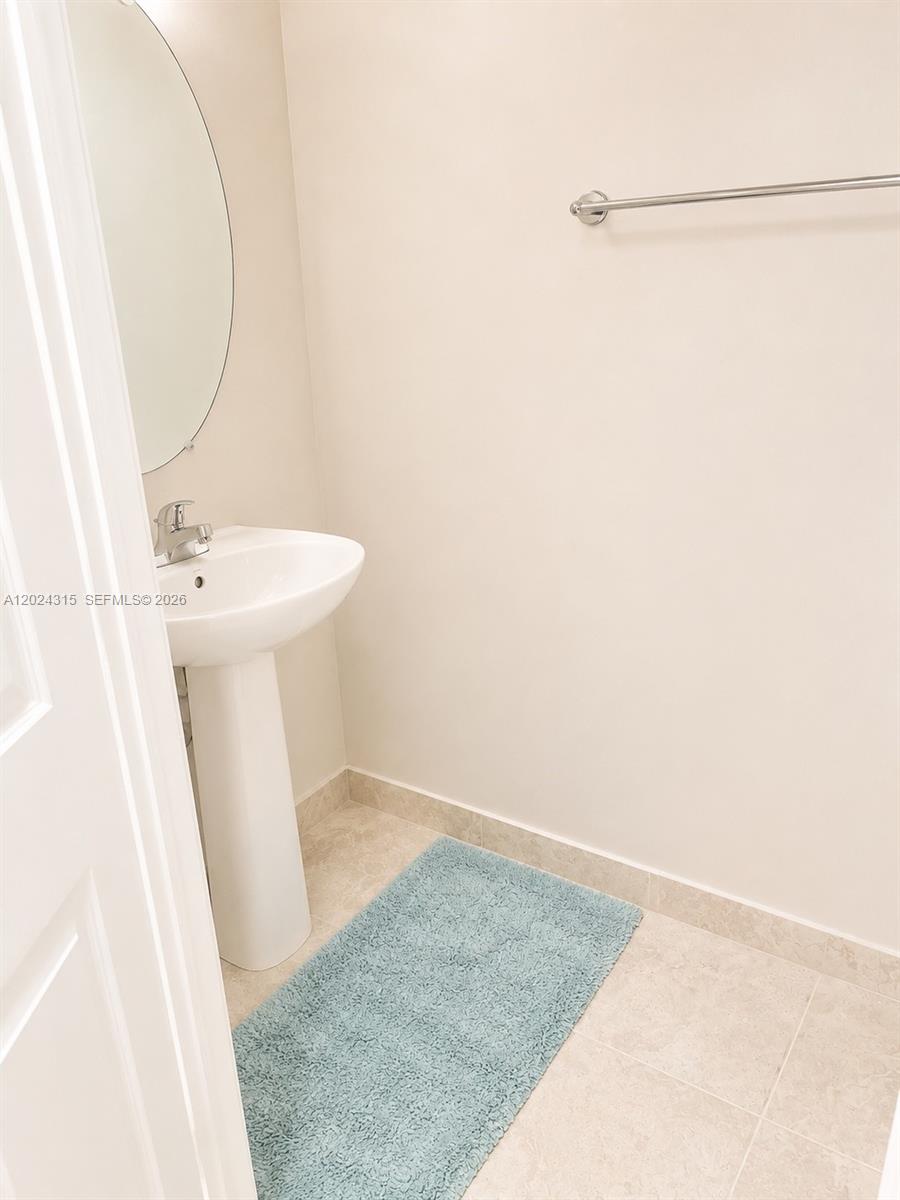 A small bathroom features a pedestal sink, a round mirror, and a light blue rug — 3327 Columbia Square Way, Fort Pierce FL 34982, FORT PIERCE, FL