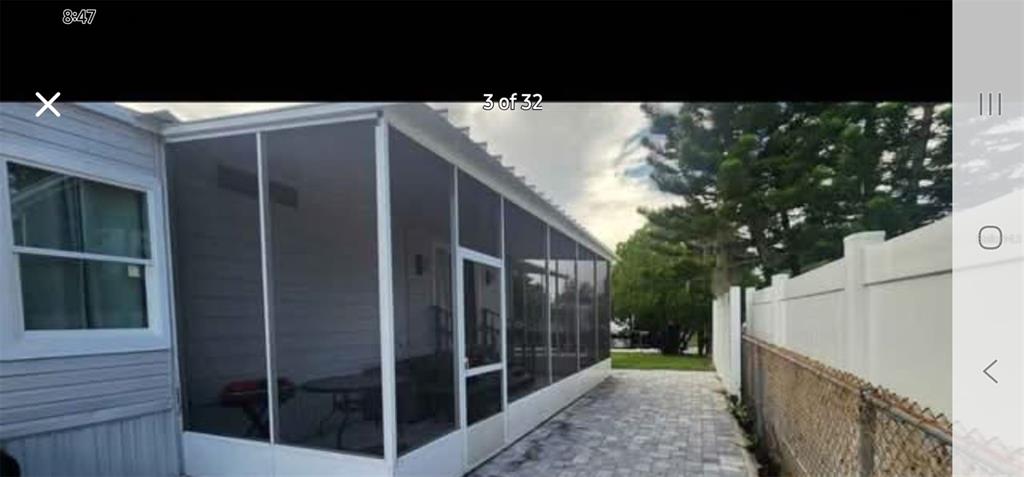 A screened-in porch with white framing sits beside a house next to a paved walkway — 6985 MEDITERRANEAN ROAD, ORLANDO, FL