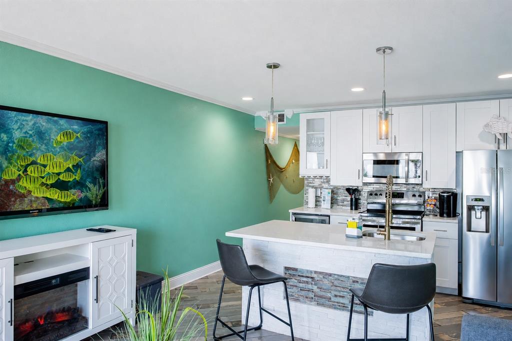 A kitchen with white cabinets, a stone-front island, and a teal accent wall with a television — 2506 N ROCKY POINT DRIVE UNIT 331, TAMPA, FL