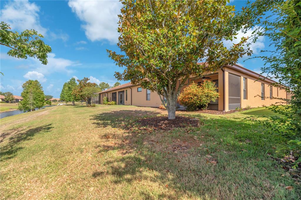 A tan house with a screened-in lanai sits on a grassy lot near a pond — 107 SHELL FALLS DRIVE, APOLLO BEACH, FL