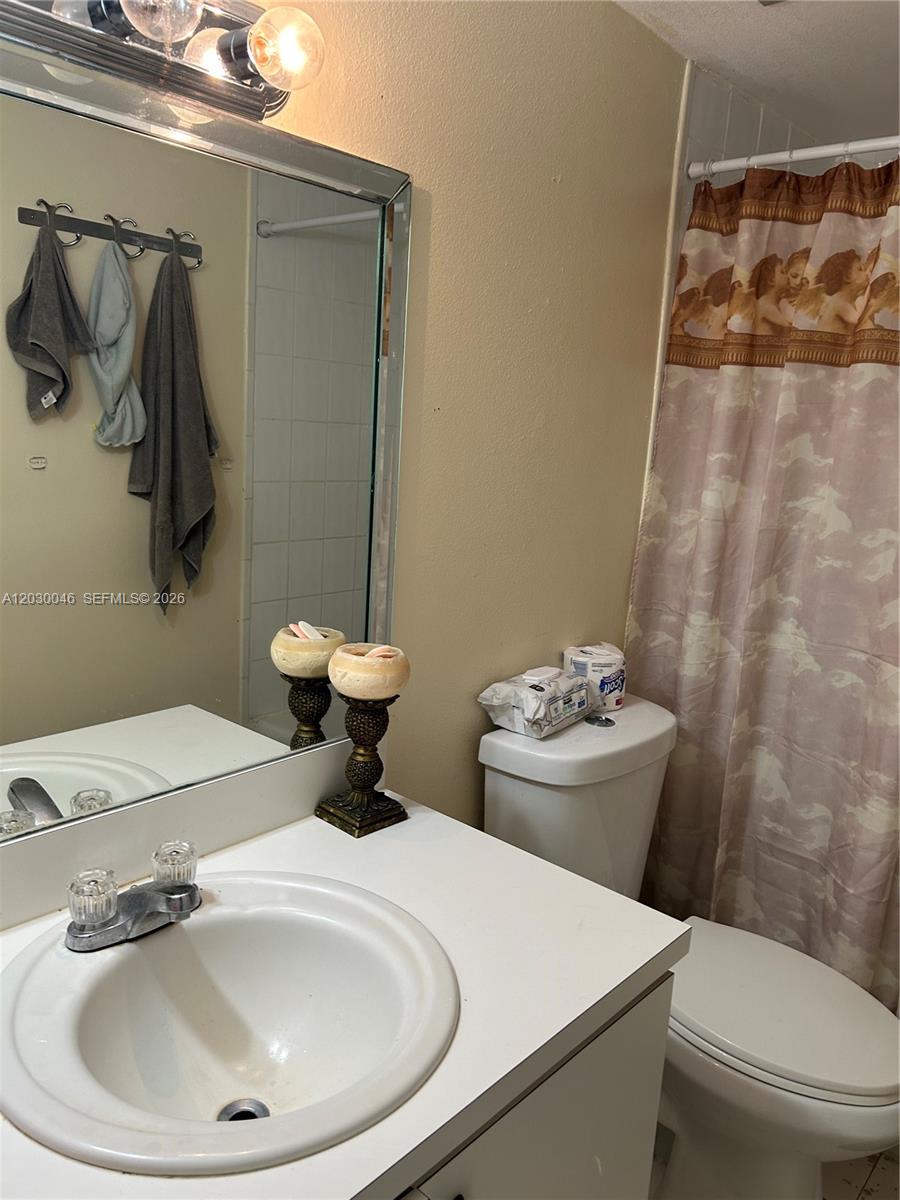 A bathroom features a white vanity, a mirror, a toilet, and a patterned shower curtain — 18051 NW 68th Ave # K104, Hialeah FL 33015, HIALEAH, FL
