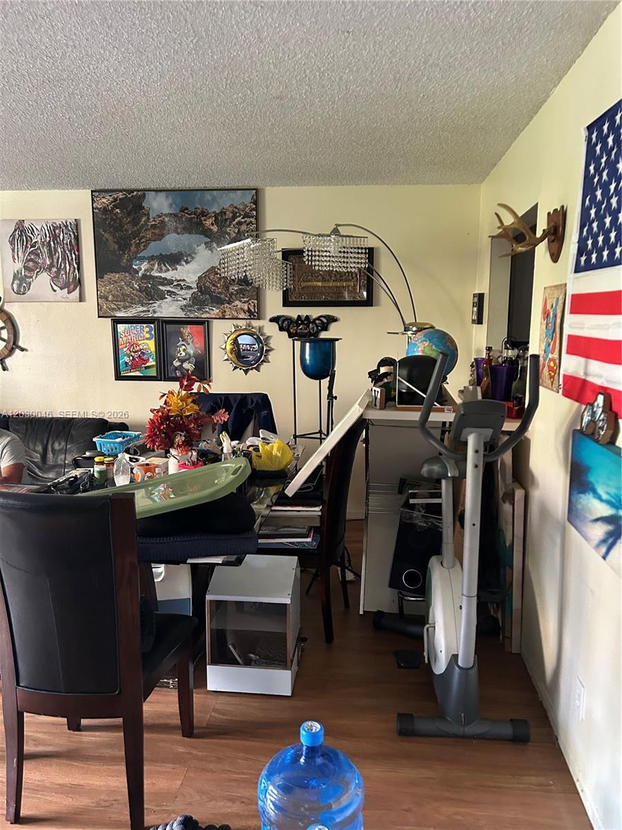 A cluttered dining area features a glass table, exercise bike, and various wall art pieces — 18051 NW 68th Ave # K104, Hialeah FL 33015, HIALEAH, FL