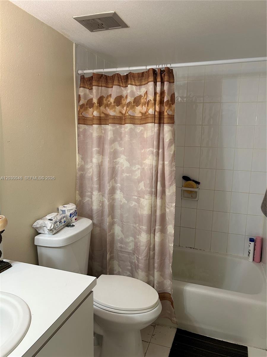 A bathroom features a white toilet, a vanity, and a shower with a patterned curtain — 18051 NW 68th Ave # K104, Hialeah FL 33015, HIALEAH, FL
