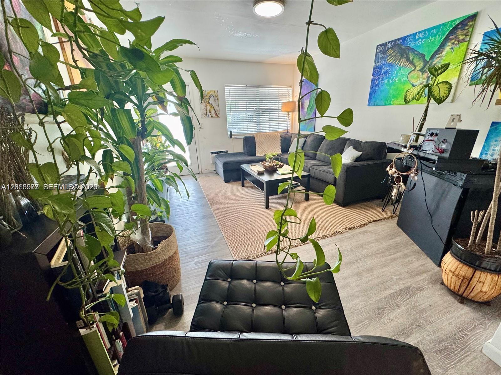 A living room features a sectional sofa, a coffee table, and several large potted plants — 330 74th St # 15, Miami Beach FL 33141, MIAMI BEACH, FL
