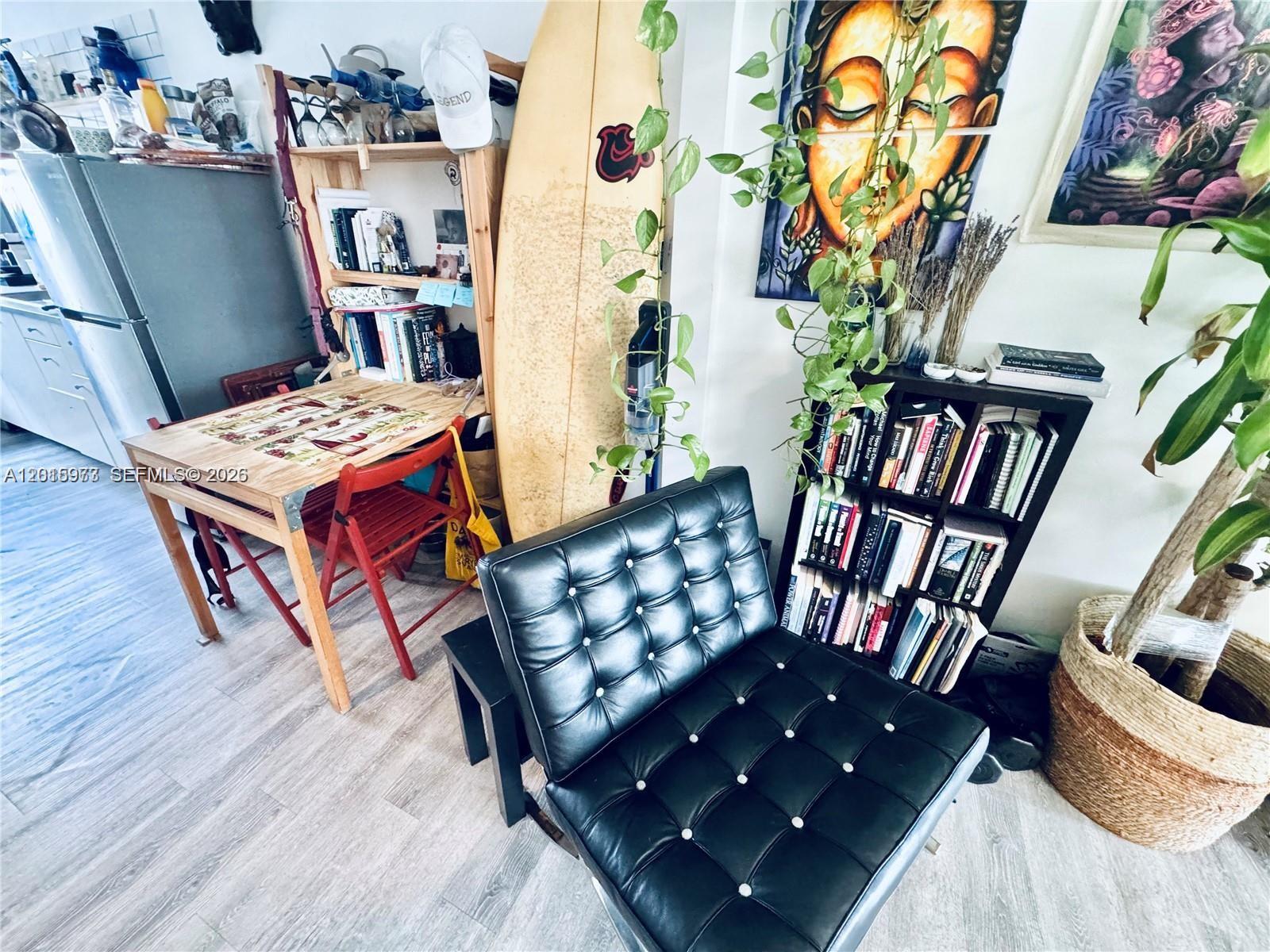 A living area features a black tufted chair, a bookshelf, a surfboard, and a dining table — 330 74th St # 15, Miami Beach FL 33141, MIAMI BEACH, FL