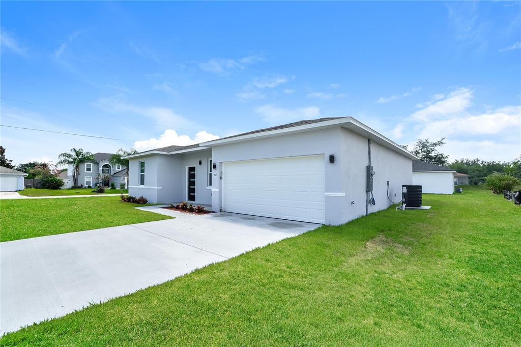 A single-story house with a white garage door, light gray stucco exterior, and a concrete driveway — 102 CONCH WAY, POINCIANA, FL