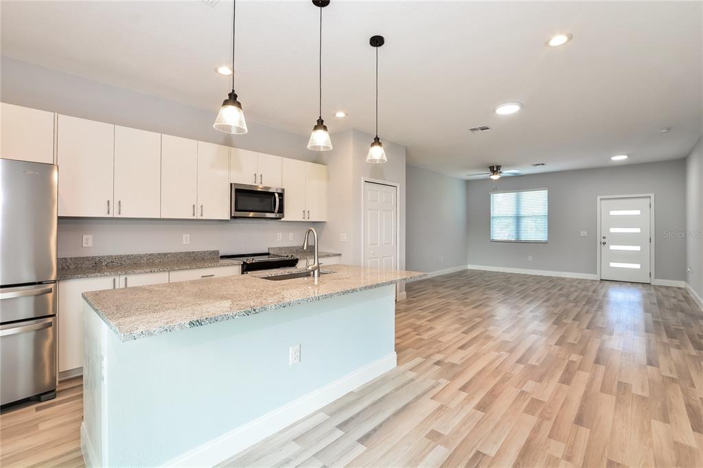 A kitchen with white cabinets and granite countertops opens into a spacious living area — 102 CONCH WAY, POINCIANA, FL