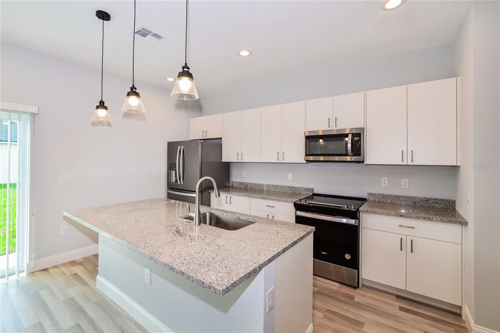 A modern kitchen features white cabinets, granite countertops, a kitchen island, and stainless steel appliances — 102 CONCH WAY, POINCIANA, FL