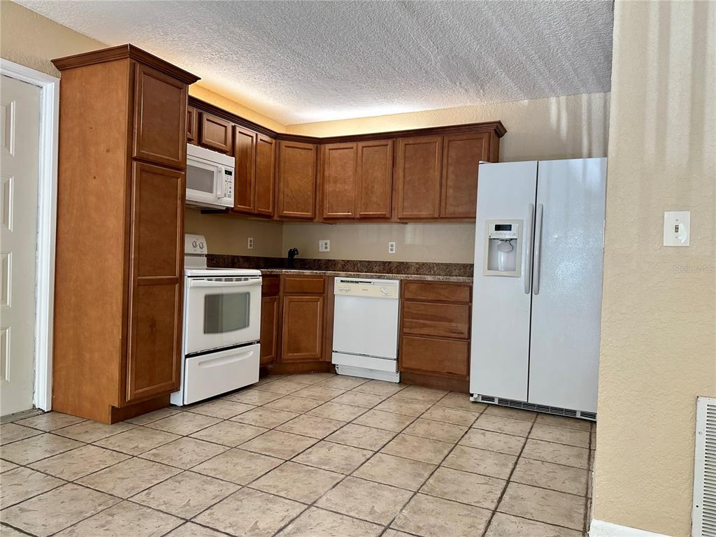 A kitchen features wood cabinets, white appliances, a tiled floor, and granite-look countertops — 8205 SUN SPRING CIRCLE UNIT B1, ORLANDO, FL