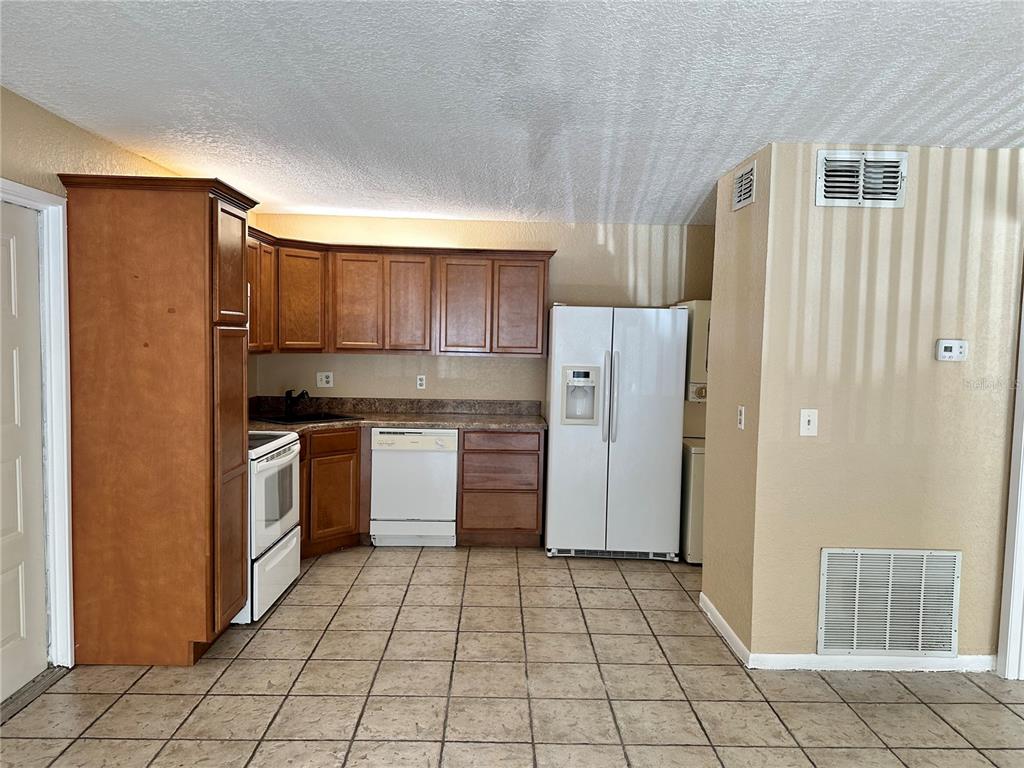 A kitchen features wood cabinets, white appliances, tiled flooring, and a side-by-side refrigerator — 8205 SUN SPRING CIRCLE UNIT B1, ORLANDO, FL