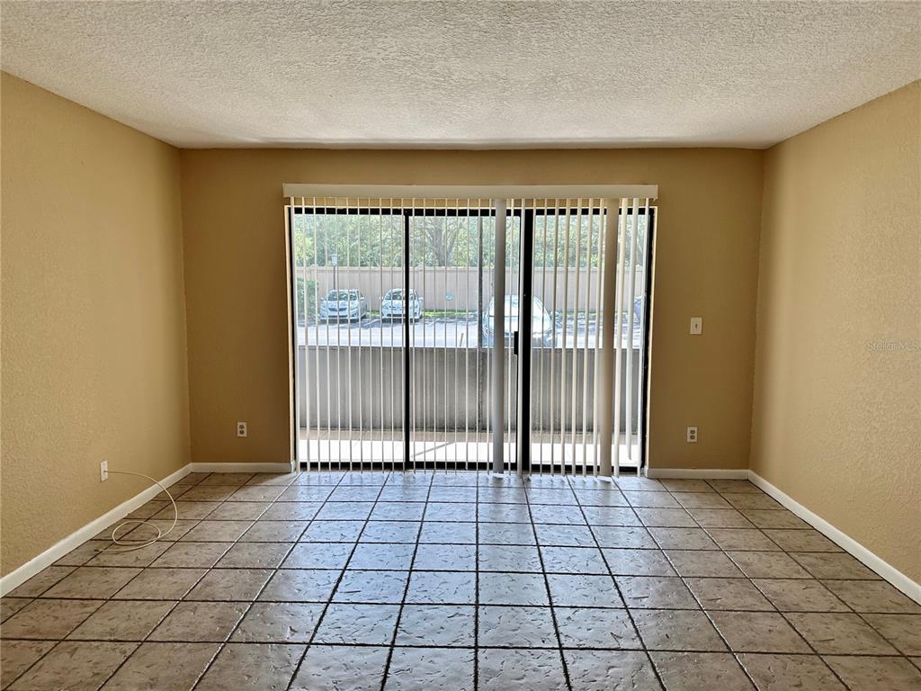 An empty room with tan walls, tiled flooring, and a large sliding glass door — 8205 SUN SPRING CIRCLE UNIT B1, ORLANDO, FL