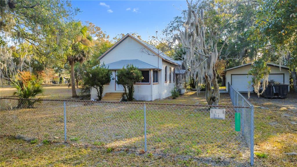 A white house with a metal roof and a detached garage sits behind a chain-link fence — 5759 LAKE STREET, MOUNT DORA, FL