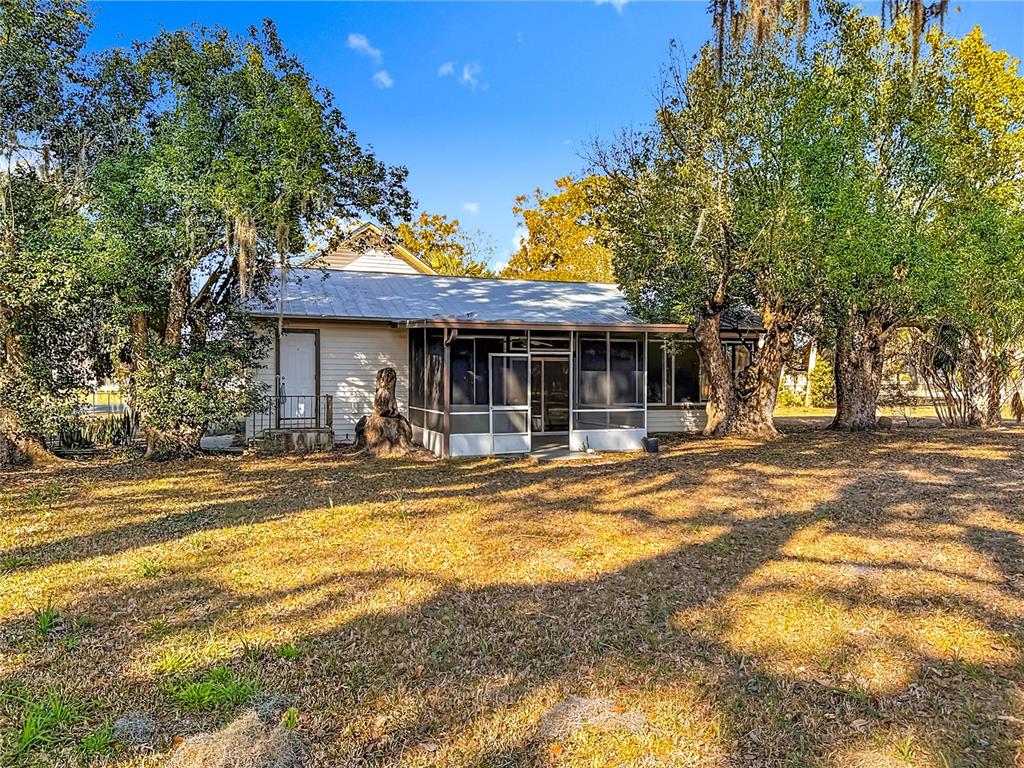 A single-story house with a screened-in porch and a metal roof sits among trees — 5759 LAKE STREET, MOUNT DORA, FL