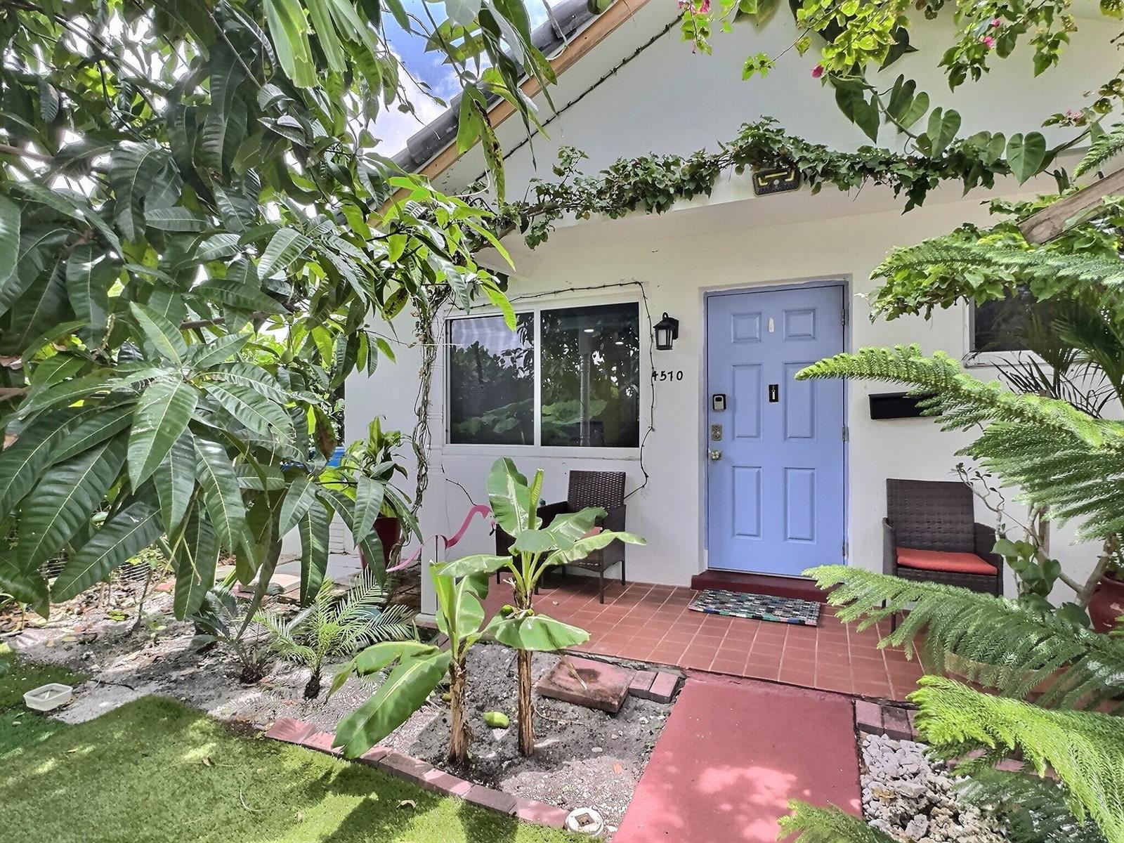 A light blue front door sits on a tiled porch surrounded by lush tropical landscaping — 4570 NW 16th Terrace, Tamarac FL 33309, TAMARAC, FL
