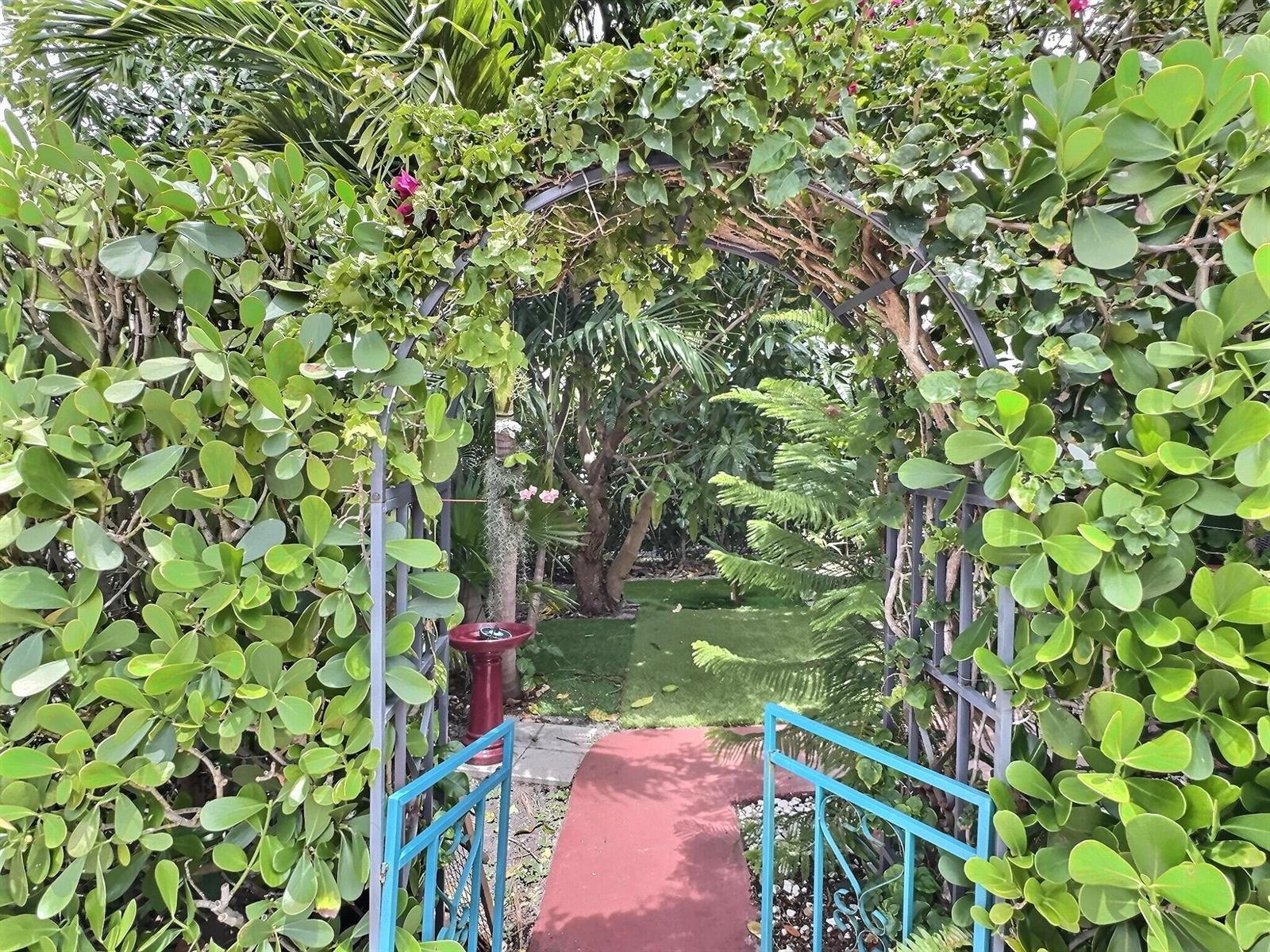 A metal garden archway leads to a path through a lush, green backyard — 4570 NW 16th Terrace, Tamarac FL 33309, TAMARAC, FL