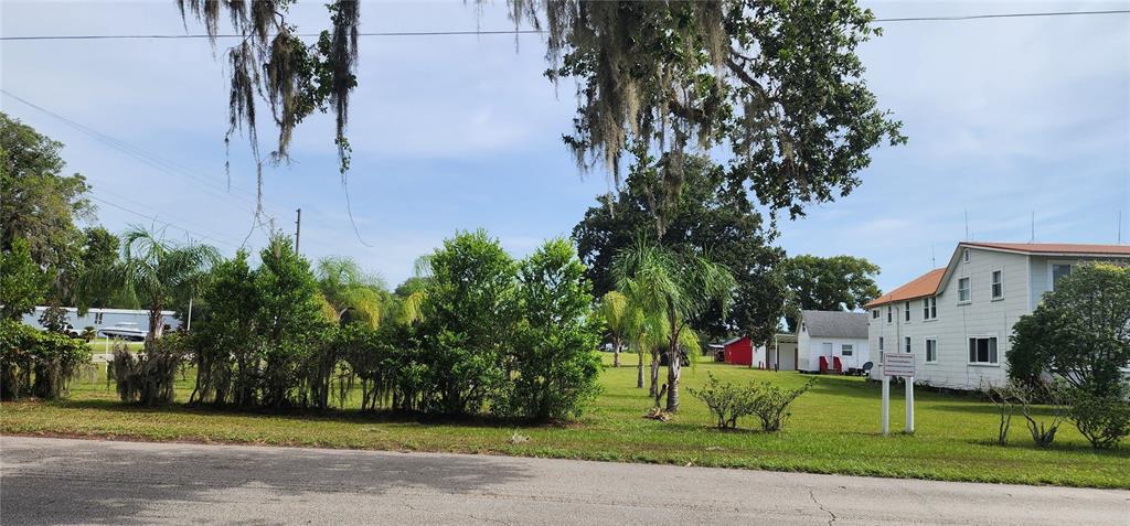 A grassy lot with trees and shrubs sits in front of a white multi-story building — 110 E 2ND AVENUE, PIERSON, FL