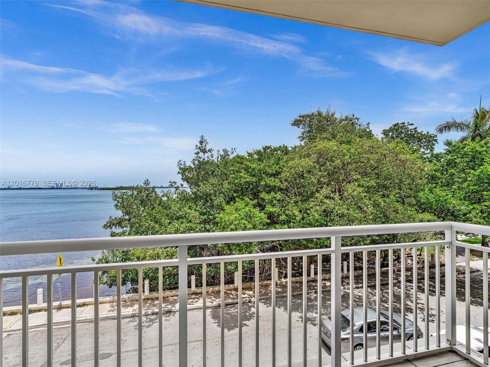 A balcony with a white railing overlooks a road, trees, and a body of water — 2000 N Bayshore Dr # 220, Miami FL 33137, MIAMI, FL