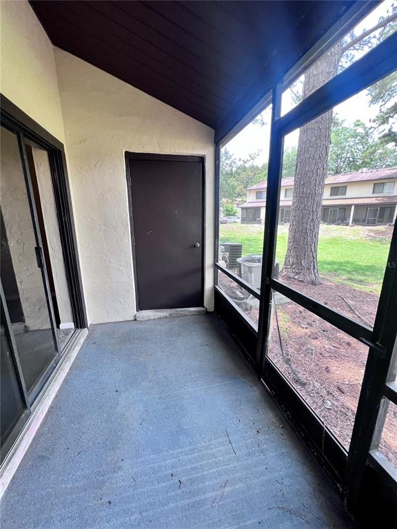 A screened-in porch features a concrete floor, a dark storage door, and sliding glass doors — 2735 SW 35TH PLACE UNIT 2004, GAINESVILLE, FL