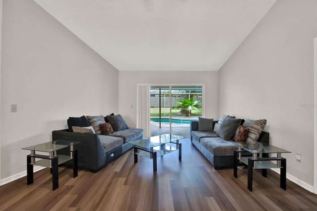 A living room with two grey sofas, glass tables, wood-look flooring, and a sliding door — 1805 TAWNEE PLACE, BRANDON, FL