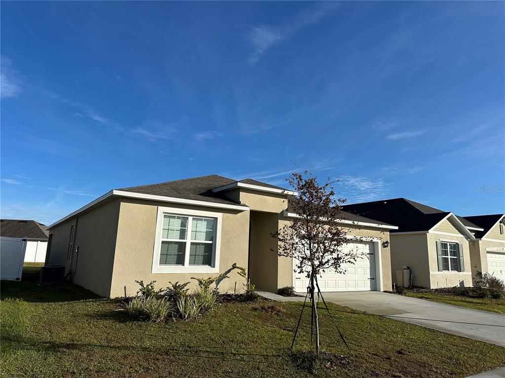 A tan, single-story suburban house with a two-car garage and a small front yard — 939 SUN BURST ROAD, WINTER HAVEN, FL