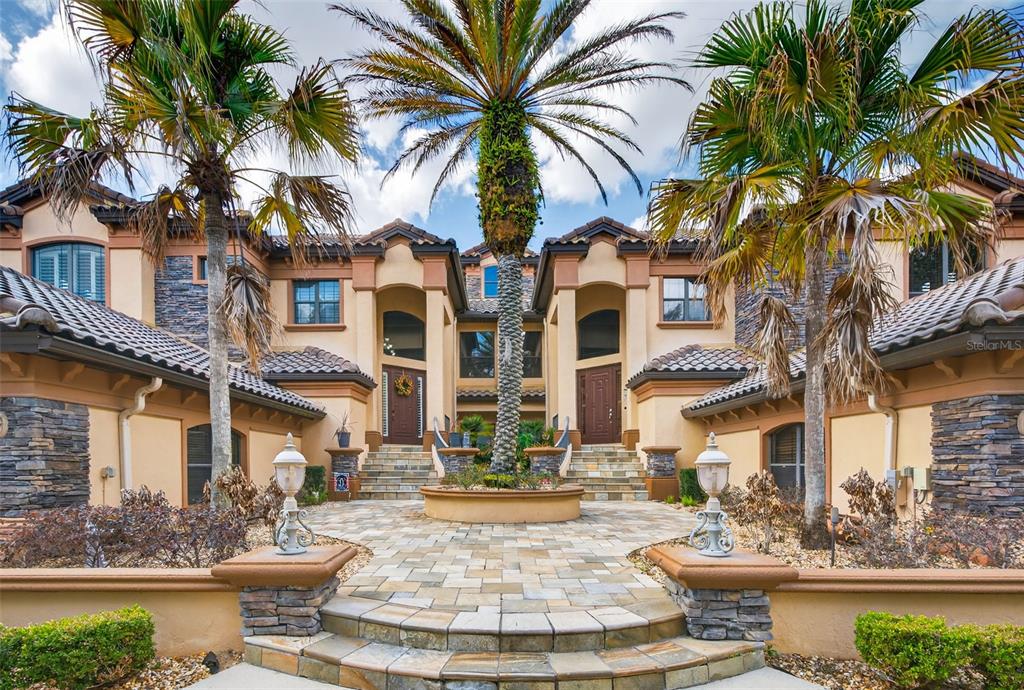 A large two-story house with a stone facade, palm trees, and a paved front courtyard — 1105 W POINTE VISTA PATH UNIT 43, HERNANDO, FL