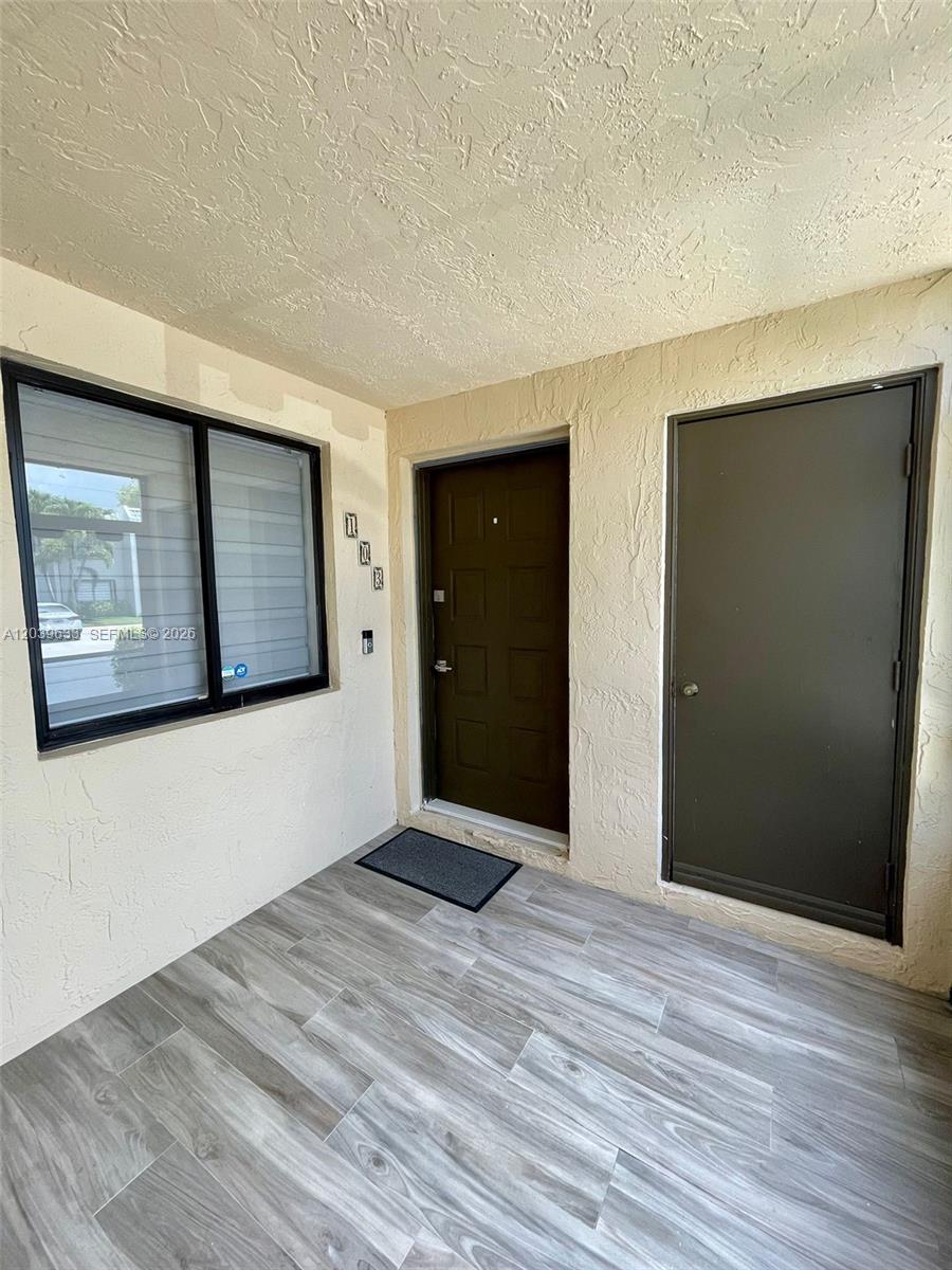An exterior entryway features a dark brown door, a window, and gray wood-look tile flooring — 16461 Blatt Blvd # 103, Weston FL 33326, WESTON, FL
