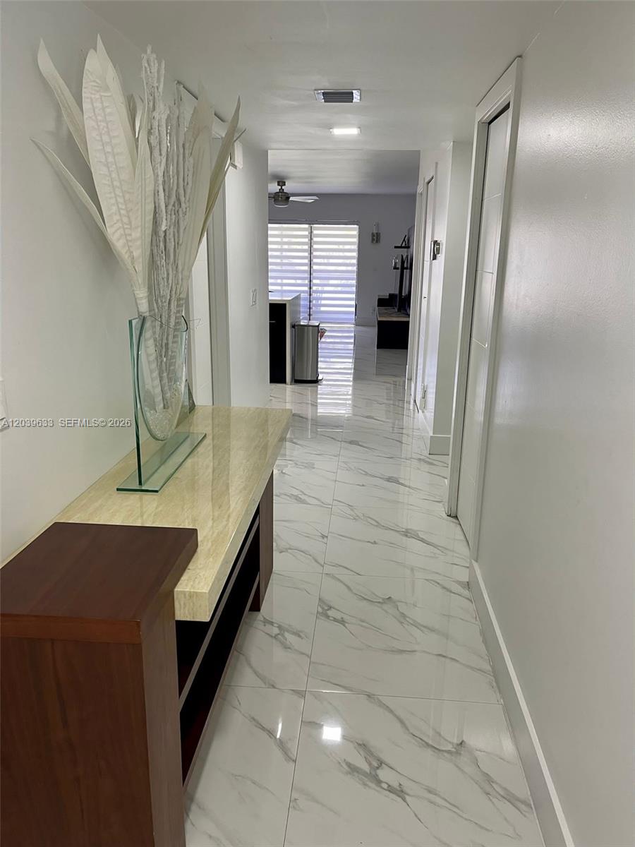 A hallway with white marble-patterned tile flooring leads toward a bright living area — 16461 Blatt Blvd # 103, Weston FL 33326, WESTON, FL
