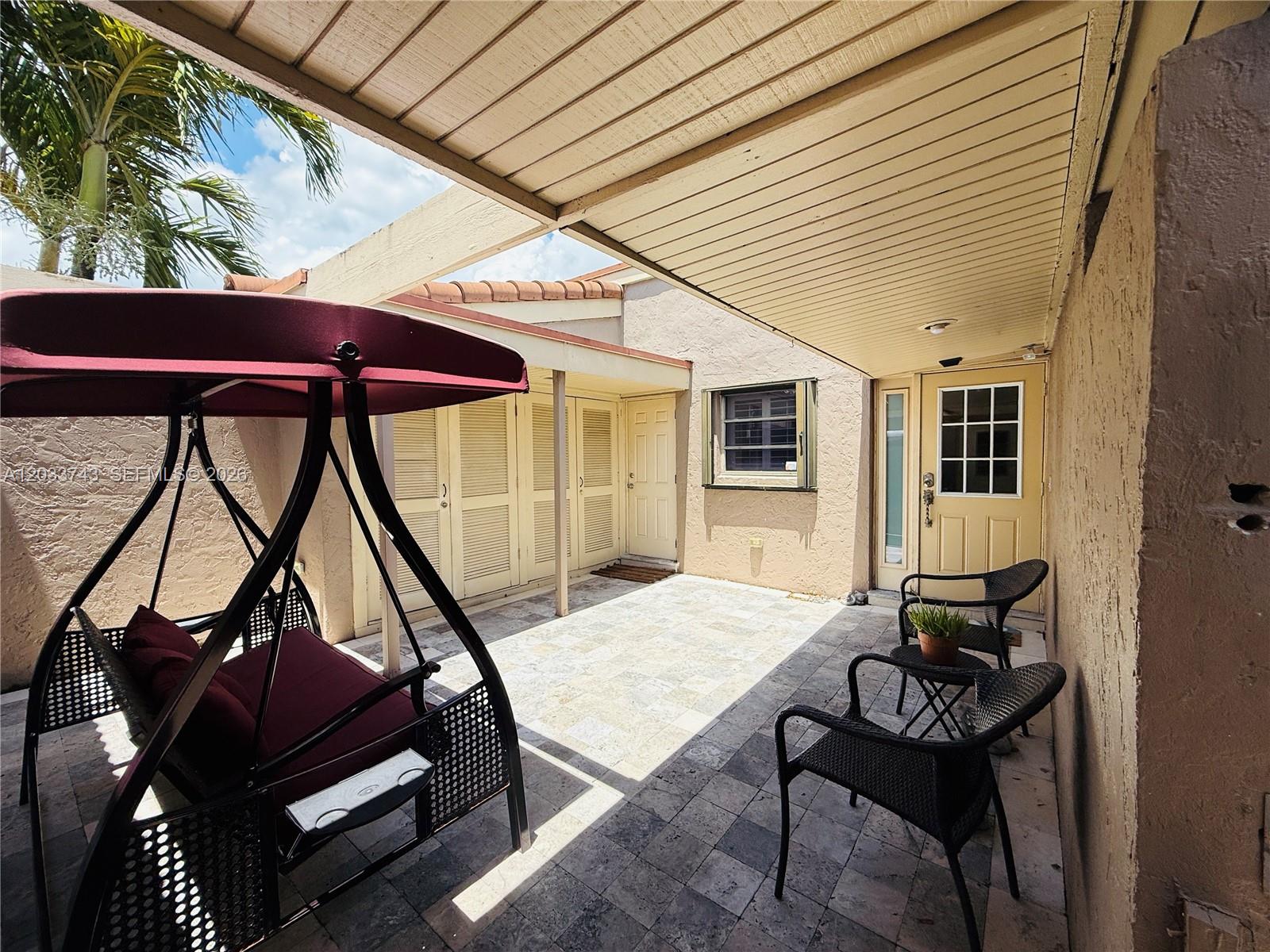 A paved patio features a covered seating area with a swing and two chairs — 103 Tweedbrook Ln # 101, Hollywood FL 33021, HOLLYWOOD, FL