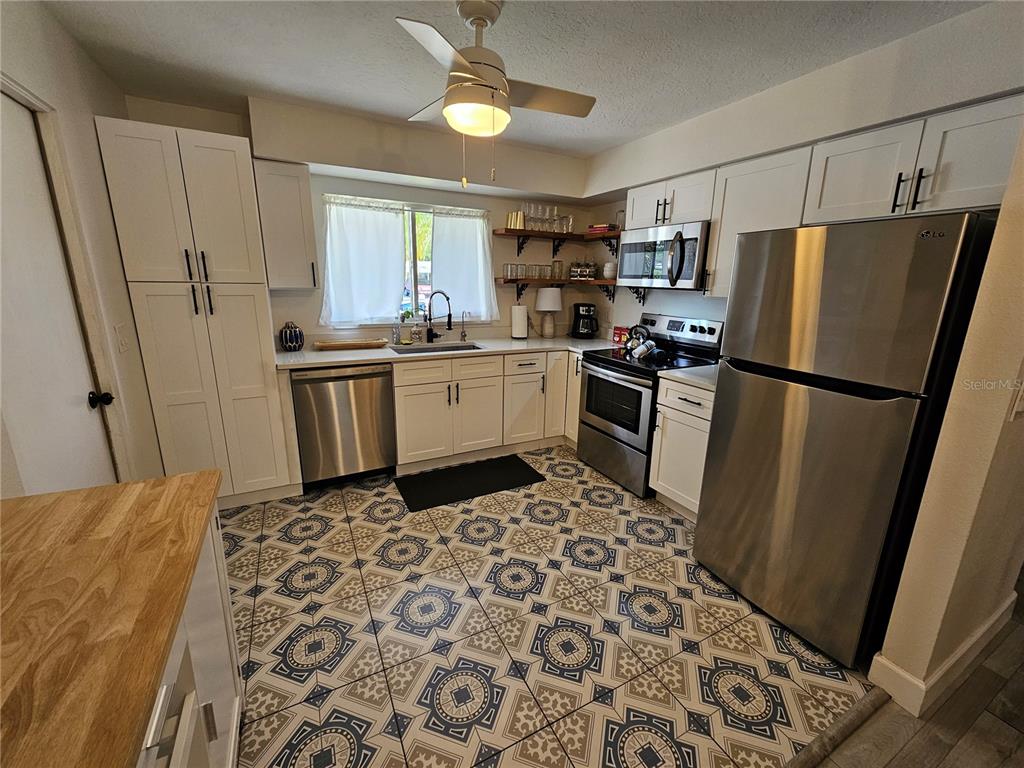A kitchen features white cabinets, stainless steel appliances, and patterned tile flooring — 6442 COLONIAL DRIVE, SARASOTA, FL