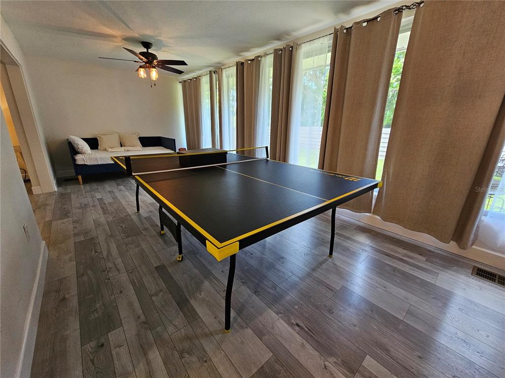 A room with wood-look flooring features a ping pong table and a daybed near windows — 6442 COLONIAL DRIVE, SARASOTA, FL