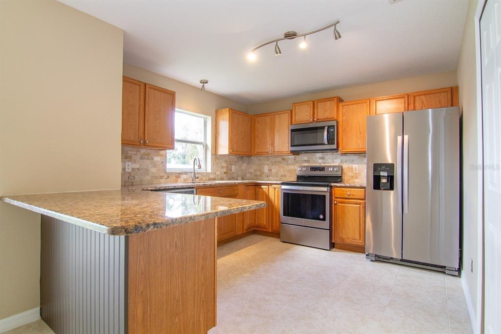 A kitchen features oak cabinets, granite countertops, stainless steel appliances, and a gray peninsula — 402 BRIDGEWATER COURT, KISSIMMEE, FL