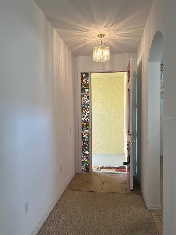 An entryway features a stained-glass sidelight, a red door, a ceiling light, and carpeted flooring — 7211 CLEOPATRA DRIVE, LAND O LAKES, FL