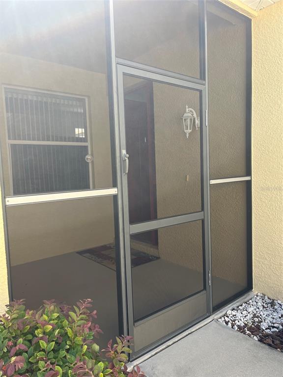 A screen door and enclosure frame the entryway to a home with a stucco exterior — 7211 CLEOPATRA DRIVE, LAND O LAKES, FL