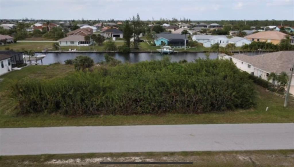 An aerial view shows a vacant, overgrown residential lot situated along a canal — 15442 MCCOMB CIRCLE, PORT CHARLOTTE, FL