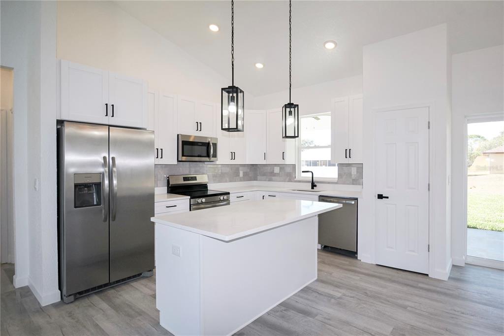A modern kitchen features white cabinets, stainless steel appliances, a center island, and gray flooring — 3915 EL RADO AVENUE, SEBRING, FL