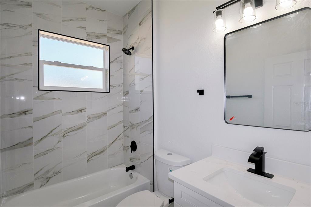 A bathroom features a white vanity, a toilet, and a bathtub with marble-patterned tile walls — 3915 EL RADO AVENUE, SEBRING, FL