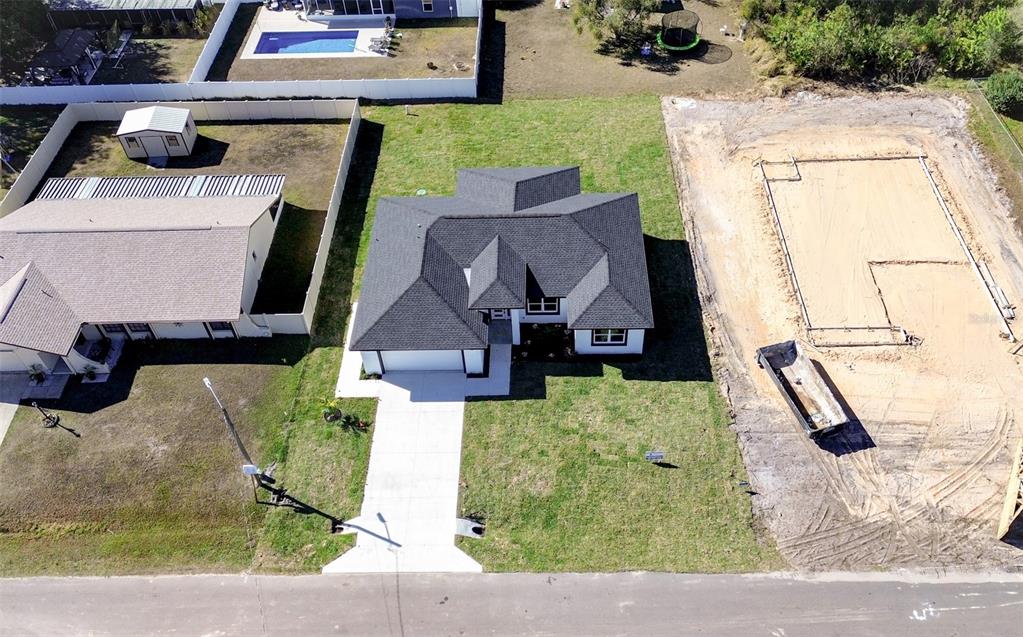 An aerial view shows a single-family house with a dark roof next to a construction site — 3915 EL RADO AVENUE, SEBRING, FL