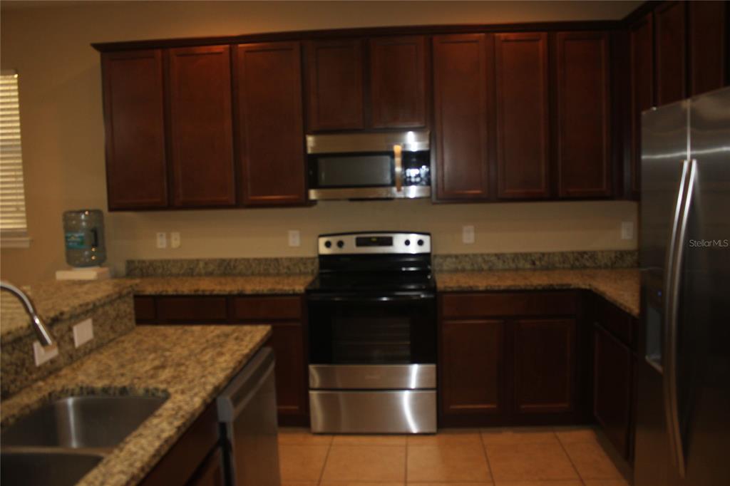 A kitchen features dark wood cabinets, granite countertops, and stainless steel appliances — 13231 OVERSTREET ROAD, WINDERMERE, FL