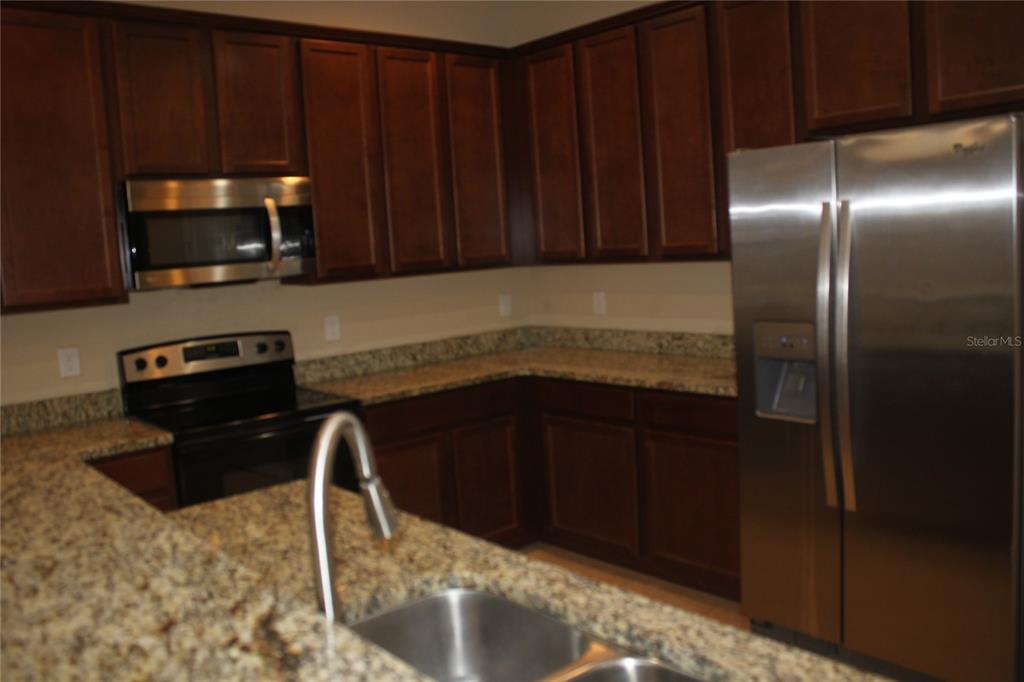 A kitchen features dark wood cabinets, granite countertops, and stainless steel appliances — 13231 OVERSTREET ROAD, WINDERMERE, FL