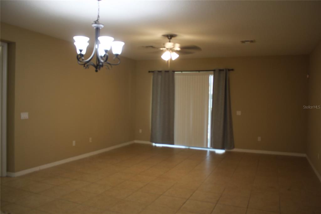 An empty room features tan tile flooring, a chandelier, a ceiling fan, and sliding doors — 13231 OVERSTREET ROAD, WINDERMERE, FL